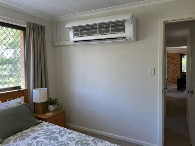 Clean split system mounted high on a bedroom wall with open front panel and visible filters in Arundel