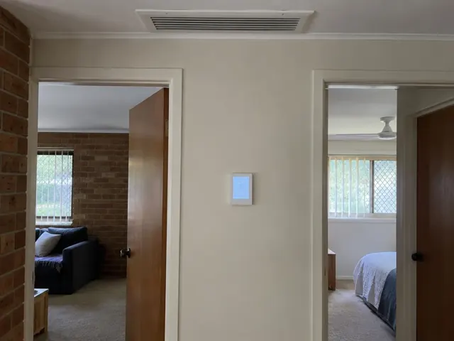 Ceiling return grille and wall controller in a beige hallway with bedrooms off either side in Ashmore
